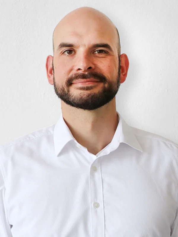 Porträt eines lächelnden Mannes mit Bart im weißen Hemd vor heller Wand, Ansprechpartner Tino Kalettka.